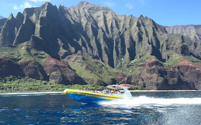 Raft speeding along NaPali Coast cliffs during afternoon snorkel tour in Hawaii.