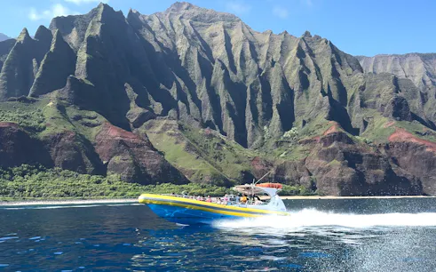 Raft speeding along NaPali Coast cliffs during afternoon snorkel tour in Hawaii.