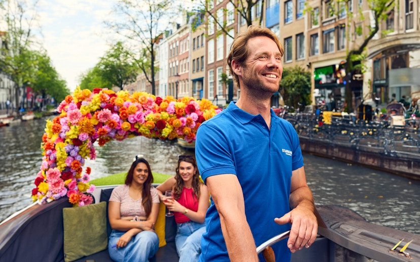 Amsterdam canal cruise on a flower-adorned boat with smiling passengers.