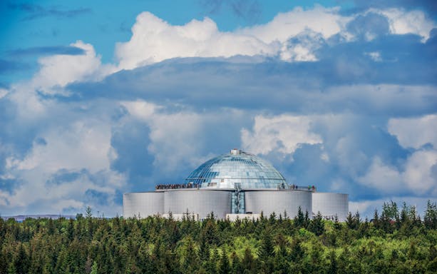 Perlan dome in Reykjavik, Iceland, surrounded by trees under a cloudy sky.