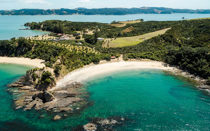 Aerial view of a scenic bay with lush greenery and clear waters in Auckland, New Zealand.