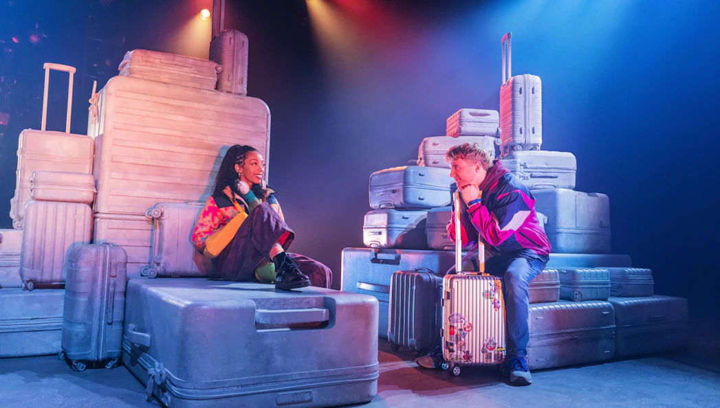 Actors surrounded by luggage in a scene from Two Strangers (Carry a Cake Across New York) Broadway show.