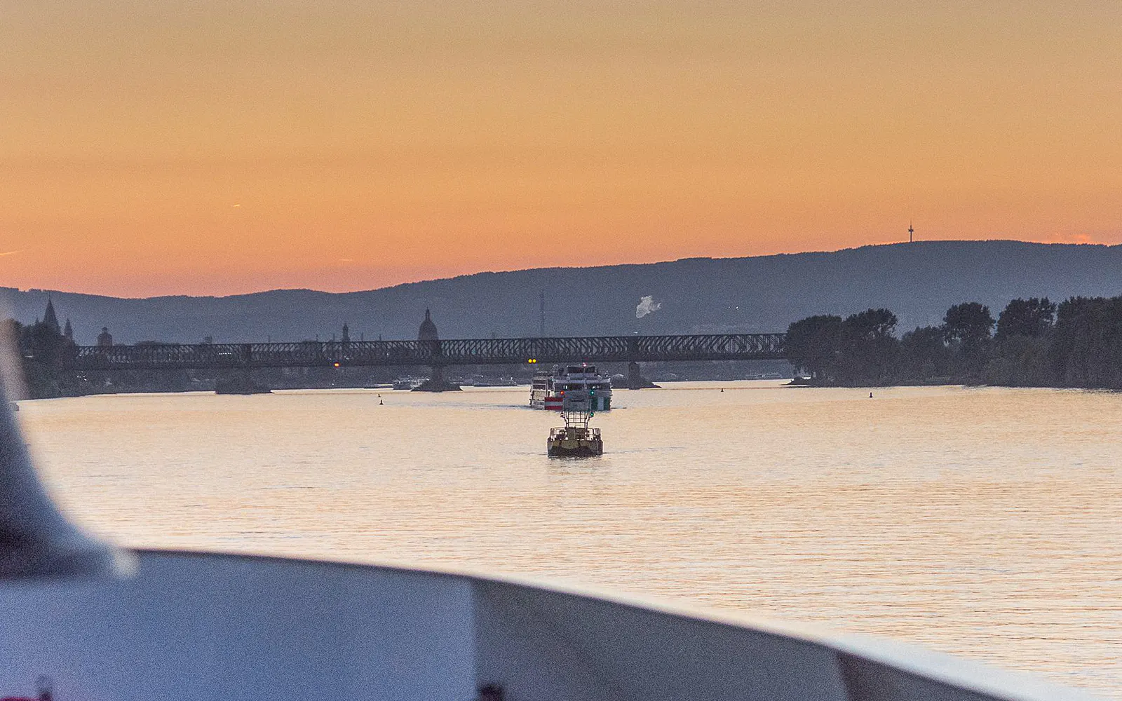 Sunset view of a river cruise approaching a bridge in Mainz, Germany.