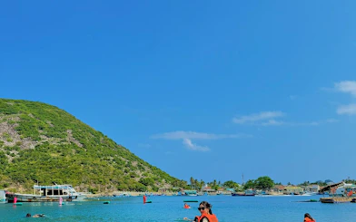 Tourists swimming near boats and lush hills on Robinson Beach, Nha Trang.