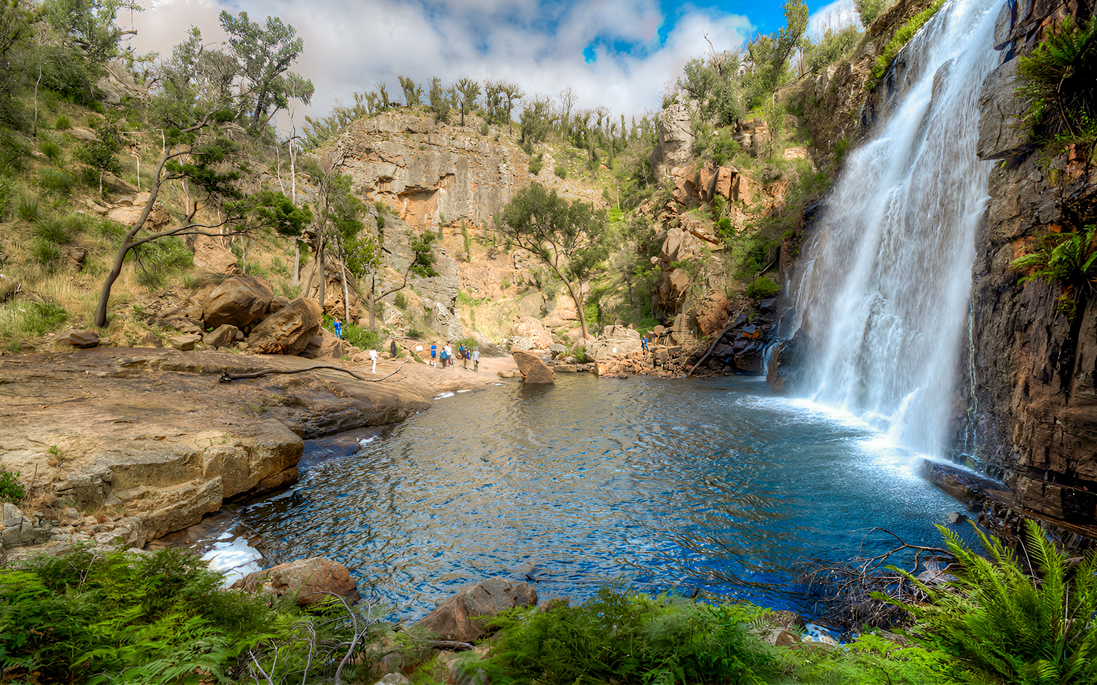 Grampians waterfall with tourists exploring rocky landscape on 1-day guided tour from Melbourne.