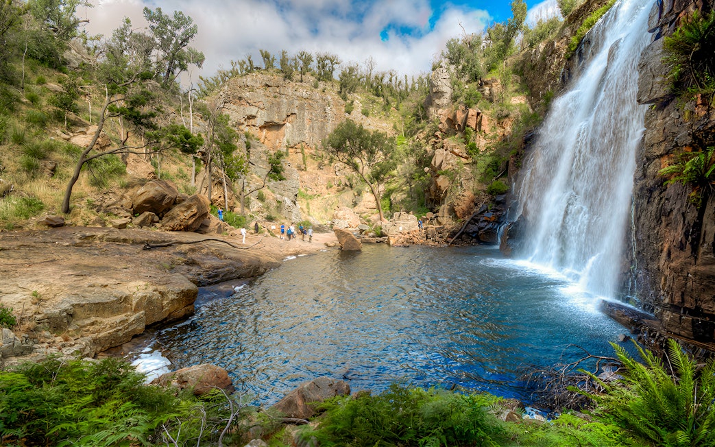 Grampians waterfall with tourists exploring rocky landscape on 1-day guided tour from Melbourne.