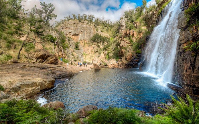Grampians waterfall with tourists exploring rocky landscape on 1-day guided tour from Melbourne.