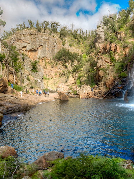 Grampians waterfall with tourists exploring rocky landscape on 1-day guided tour from Melbourne.