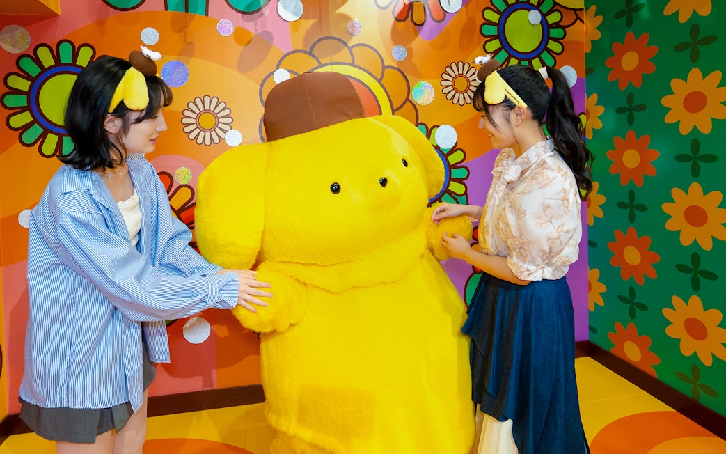Visitors interacting with a large yellow character at Sanrio Puroland.