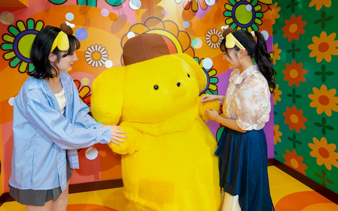 Visitors interacting with a large yellow character at Sanrio Puroland.