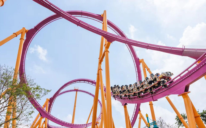 Roller coaster at Chimelong Paradise with riders on a loop under a blue sky.