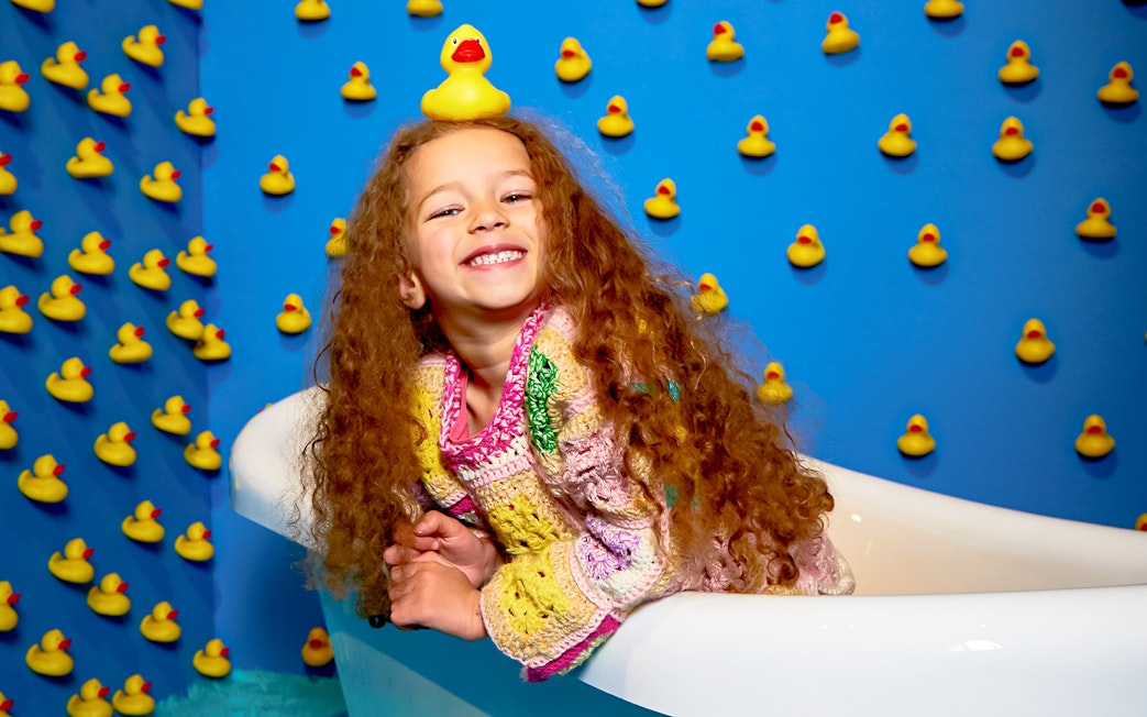 Child smiling in a bathtub surrounded by rubber ducks at Bubble Planet, Washington DC.