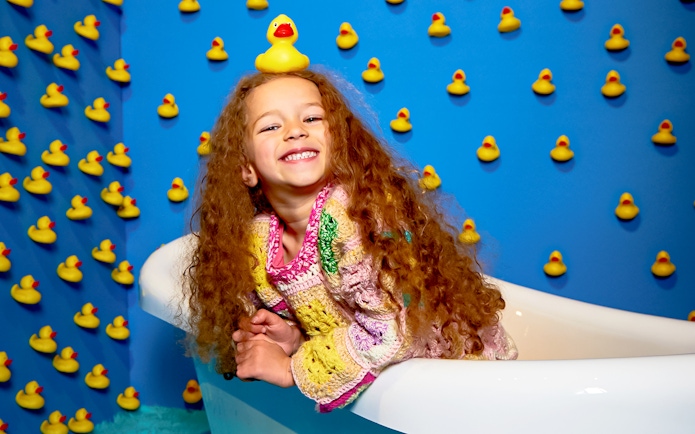 Child smiling in a bathtub surrounded by rubber ducks at Bubble Planet, Washington DC.