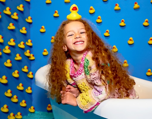 Child smiling in a bathtub surrounded by rubber ducks at Bubble Planet, Washington DC.