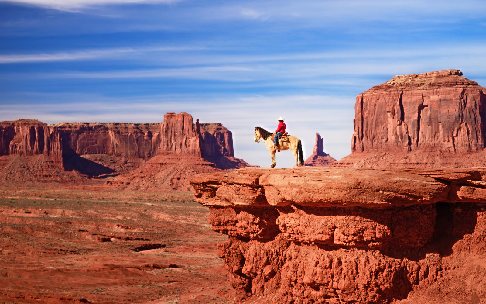 Native American on horseback overlooking Monument Valley's red rock formations.