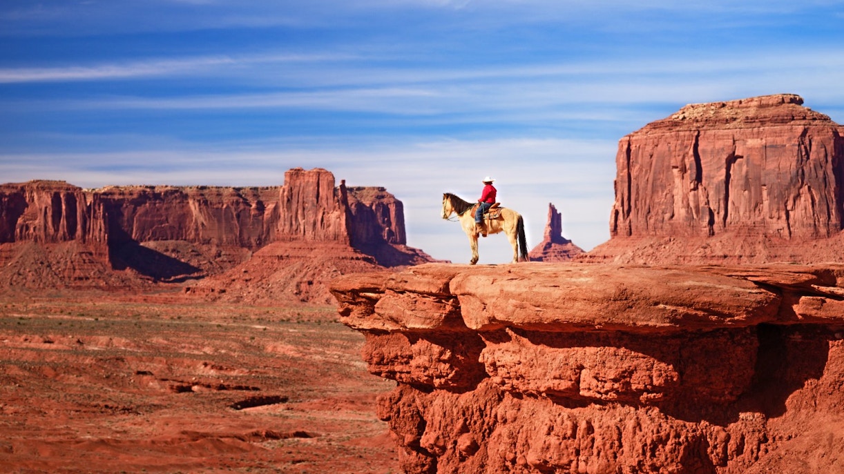 Native American on horseback overlooking Monument Valley's red rock formations.