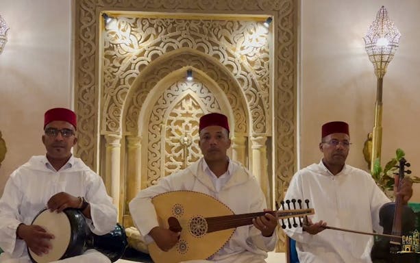 Musicians in traditional Moroccan attire playing instruments in a decorated setting.