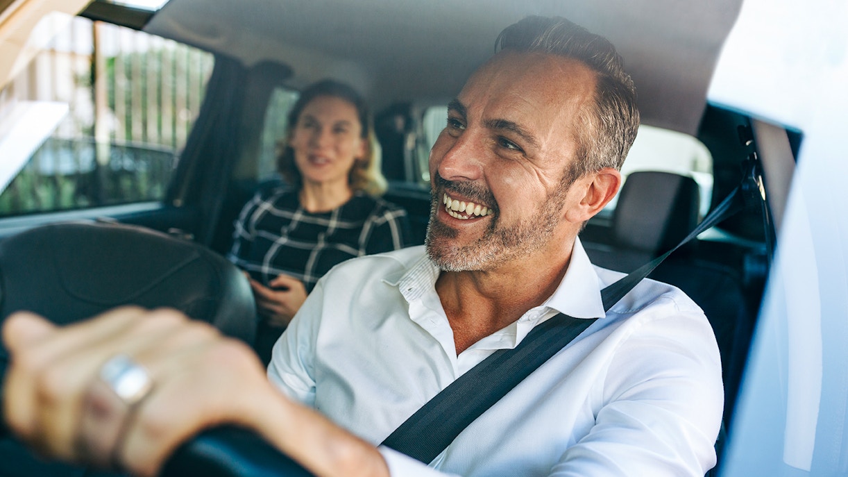 Smiling taxi driver with passenger in the back seat.