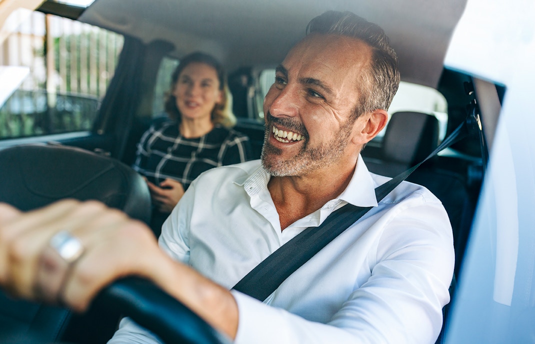 Smiling taxi driver with passenger in the back seat.