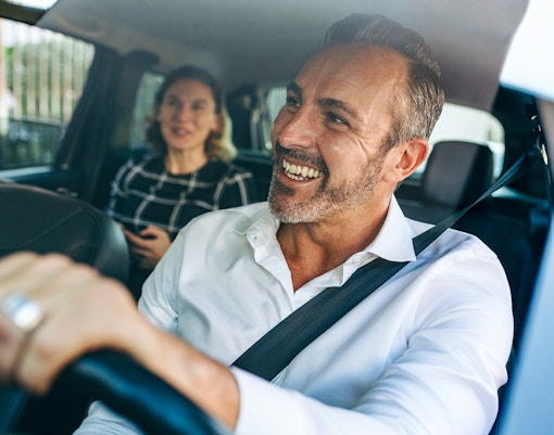Smiling taxi driver with passenger in the back seat.