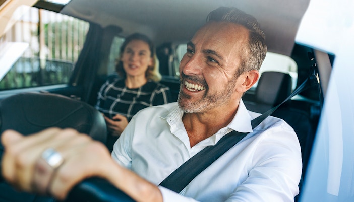 Smiling taxi driver with passenger in the back seat.