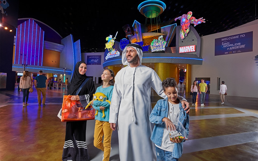 Family at IMG Worlds of Adventure entrance with superhero statues, Dubai.