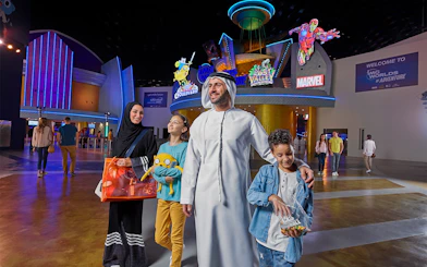 Family at IMG Worlds of Adventure entrance with superhero statues, Dubai.