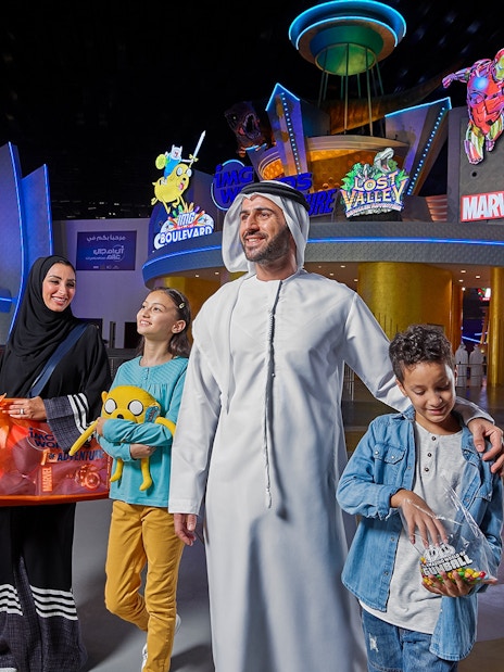 Family at IMG Worlds of Adventure entrance with superhero statues, Dubai.