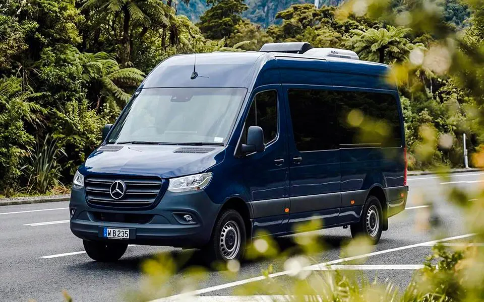 Tour van on scenic road to Milford Sound, surrounded by lush greenery.