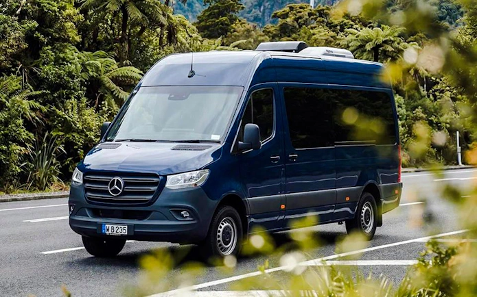 Tour van on scenic road to Milford Sound, surrounded by lush greenery.