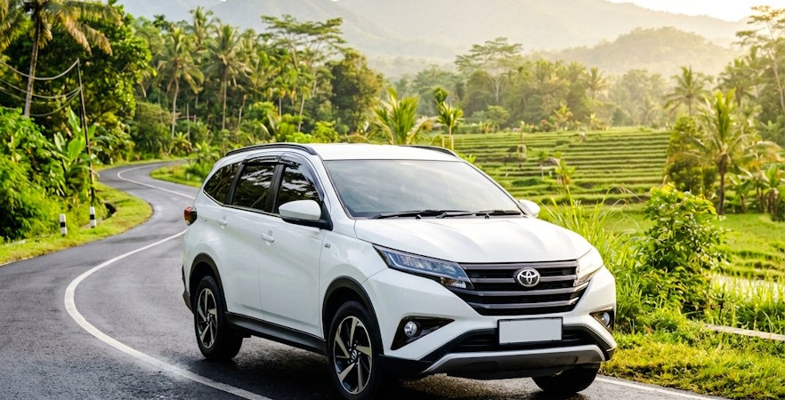 Toyota Rush on a scenic winding road with lush greenery and mountains in the background.