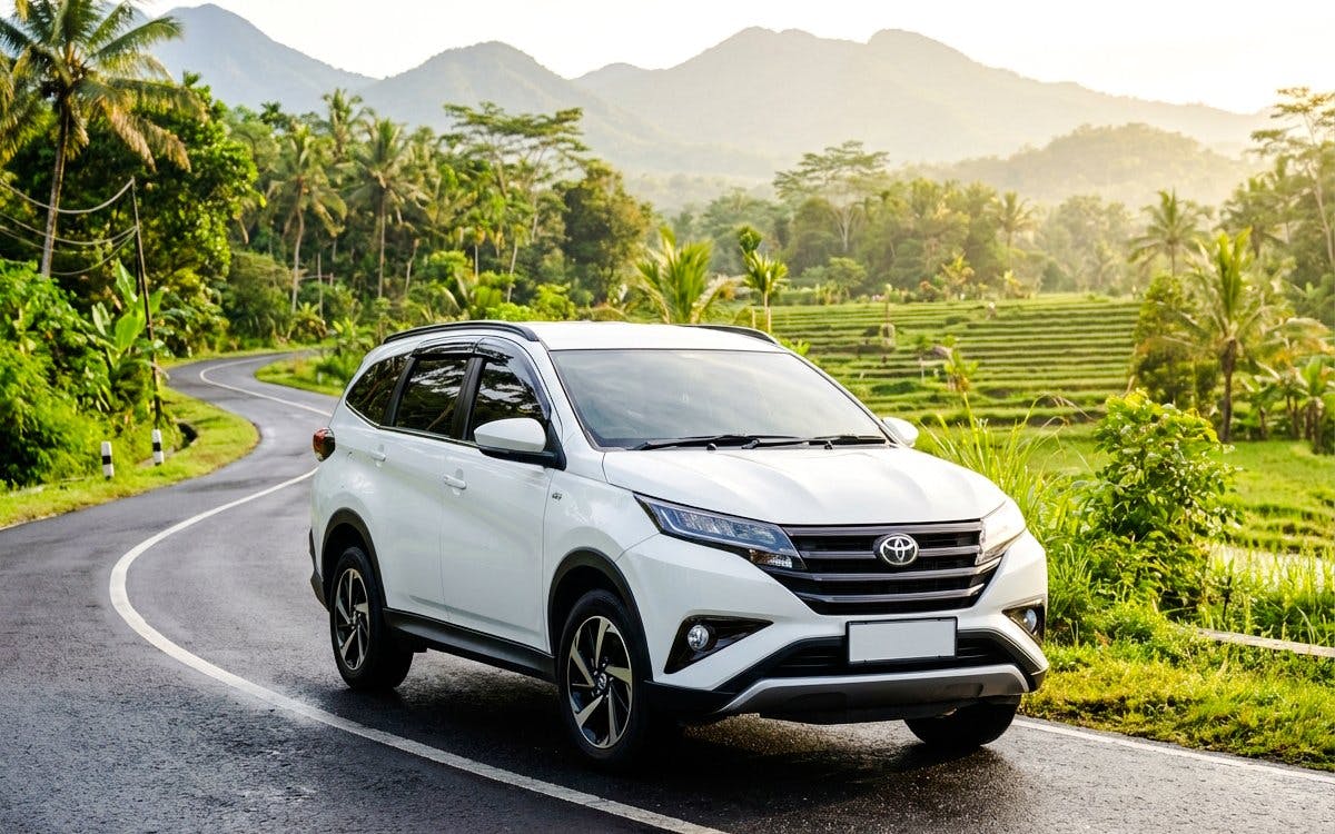 Toyota Rush on a scenic winding road with lush greenery and mountains in the background.