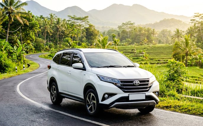 Toyota Rush on a scenic winding road with lush greenery and mountains in the background.