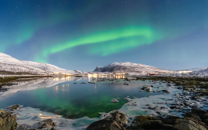 Northern lights over snowy mountains and a reflective lake in Tromso, Norway.