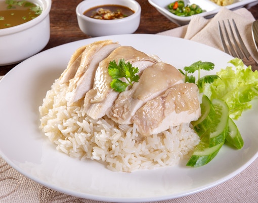 Hainanese chicken rice with sliced chicken, rice, cucumber, and cilantro on a white plate.