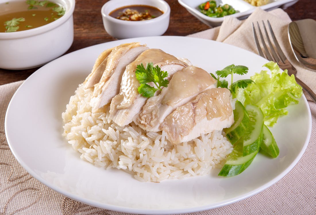 Hainanese chicken rice served with sliced chicken, rice, and dipping sauces.