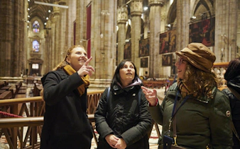 Tourists with guide inside Milan Duomo, admiring architecture and stained glass.