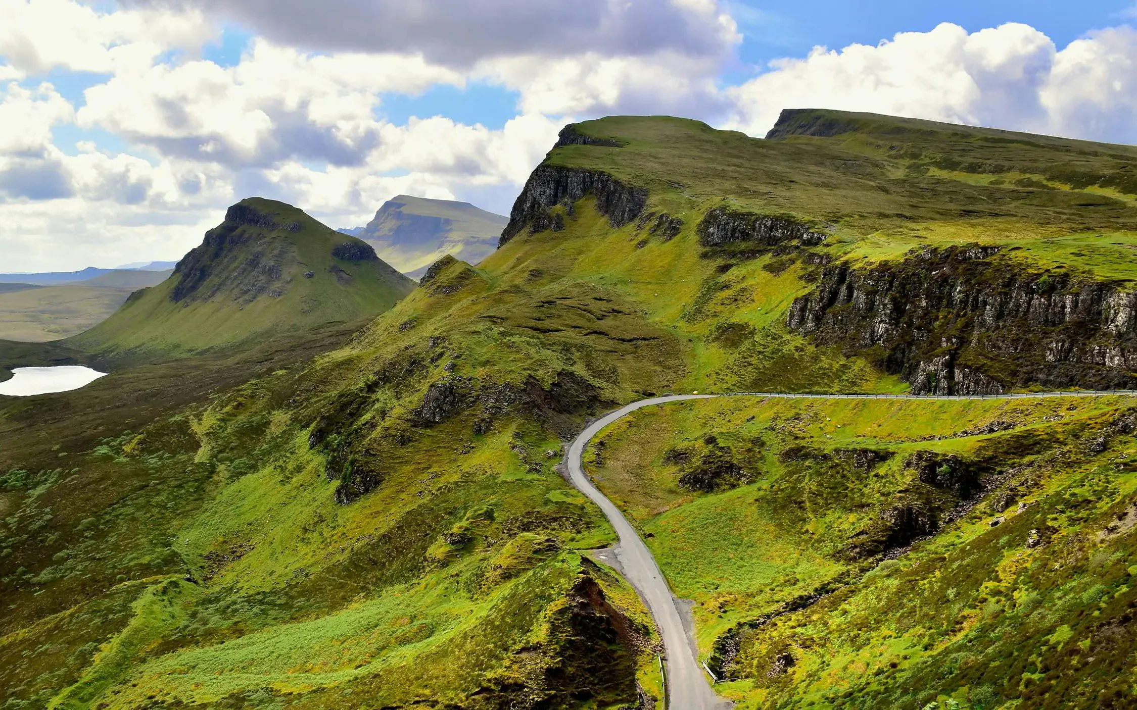 Winding road through Trotternish Ridge on the Isle of Skye, surrounded by lush green hills.