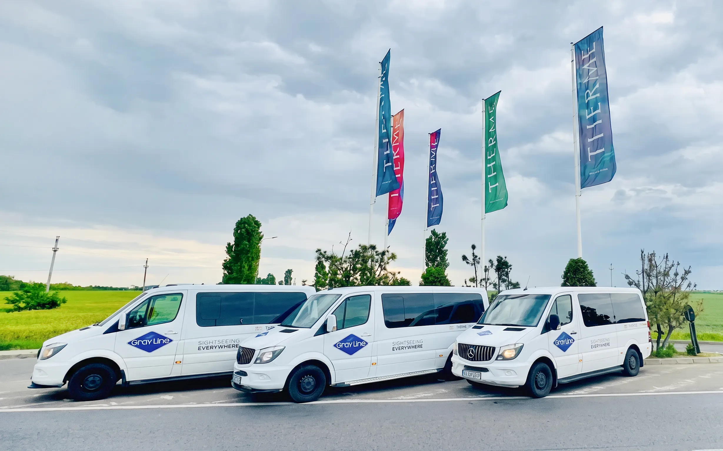 Shuttle vans parked at Therme Bucuresti with colorful flags in the background.