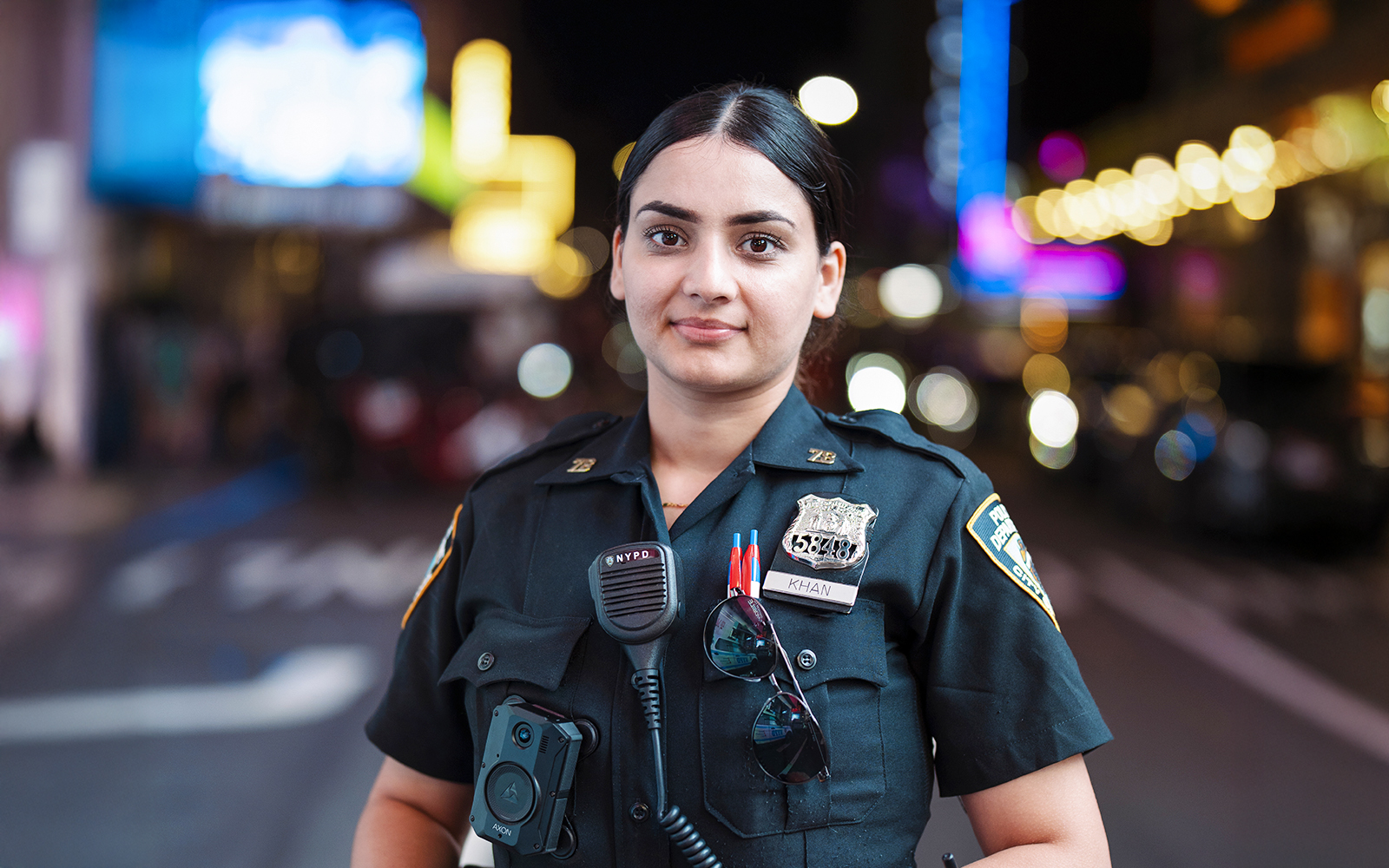 Police officer in uniform at Times Square, New York City, with bright lights in the background.