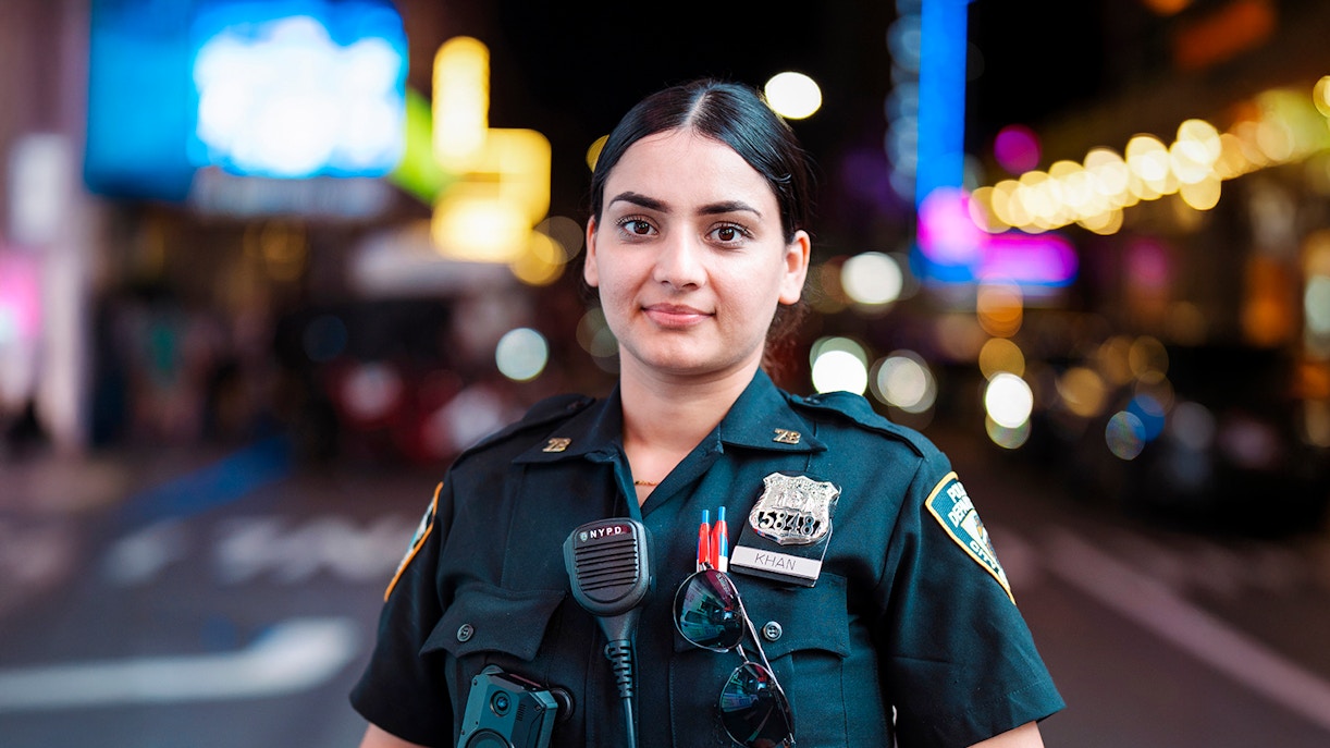 Police officer in uniform at Times Square, New York City, with bright lights in the background.
