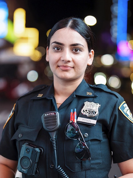 Police officer in uniform at Times Square, New York City, with bright lights in the background.