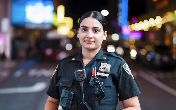 Police officer in uniform at Times Square, New York City, with bright lights in the background.