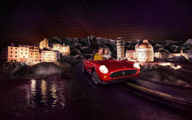 Visitors in a red Ferrari ride past miniature Italian landmarks at Ferrari World Abu Dhabi.