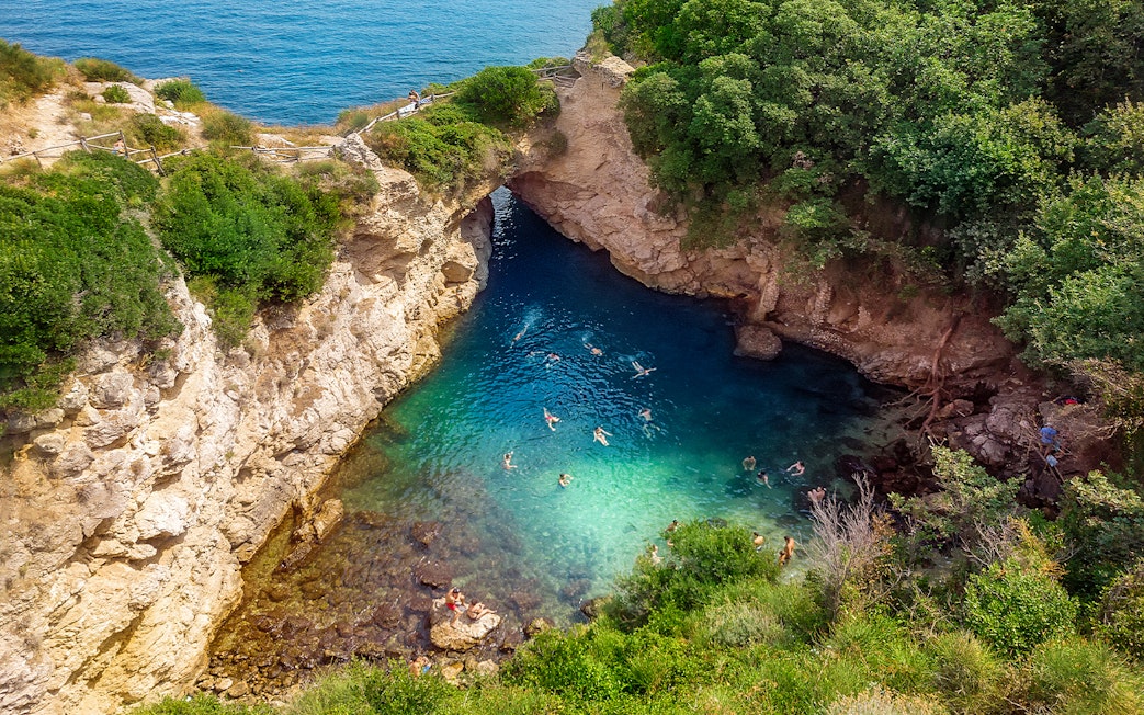 People swimming in Regina Giovanna Queen's Bath, Sorrento, Italy, surrounded by rocky cliffs.