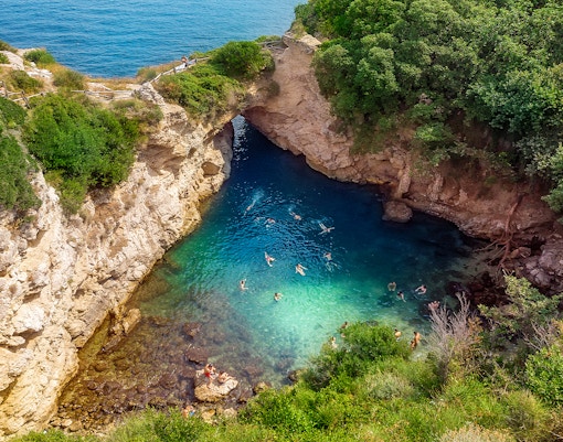 People swimming in Regina Giovanna Queen's Bath, Sorrento, Italy, surrounded by rocky cliffs.