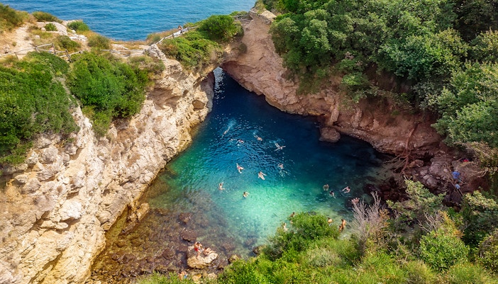 People swimming in Regina Giovanna Queen's Bath, Sorrento, Italy, surrounded by rocky cliffs.