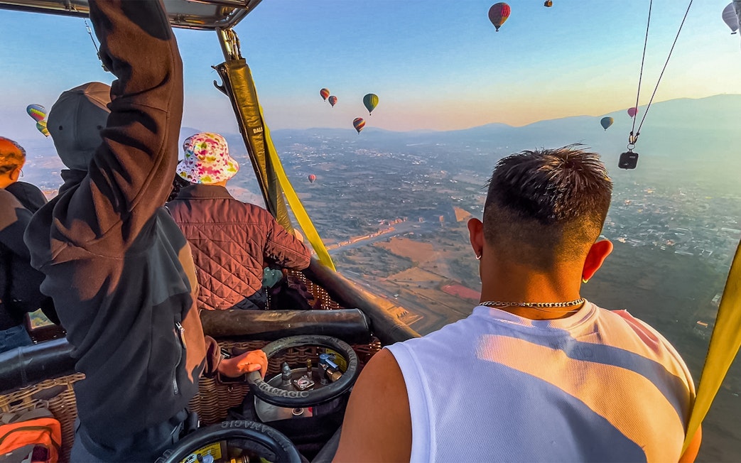 Passengers in a hot air balloon over Teotihuacan pyramids, Mexico, with other balloons in the sky.