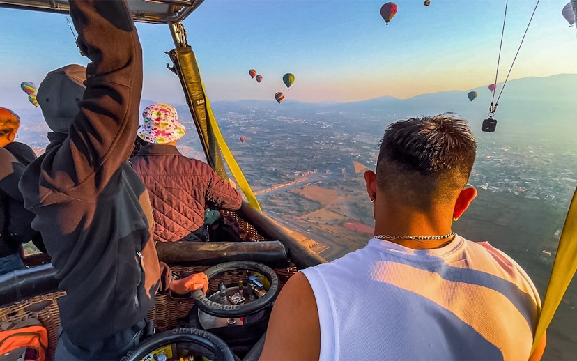 Passengers in a hot air balloon over Teotihuacan pyramids, Mexico, with other balloons in the sky.