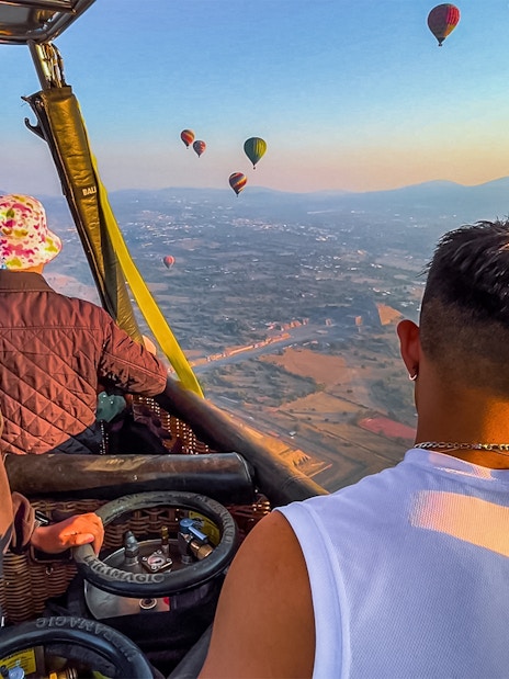 Passengers in a hot air balloon over Teotihuacan pyramids, Mexico, with other balloons in the sky.